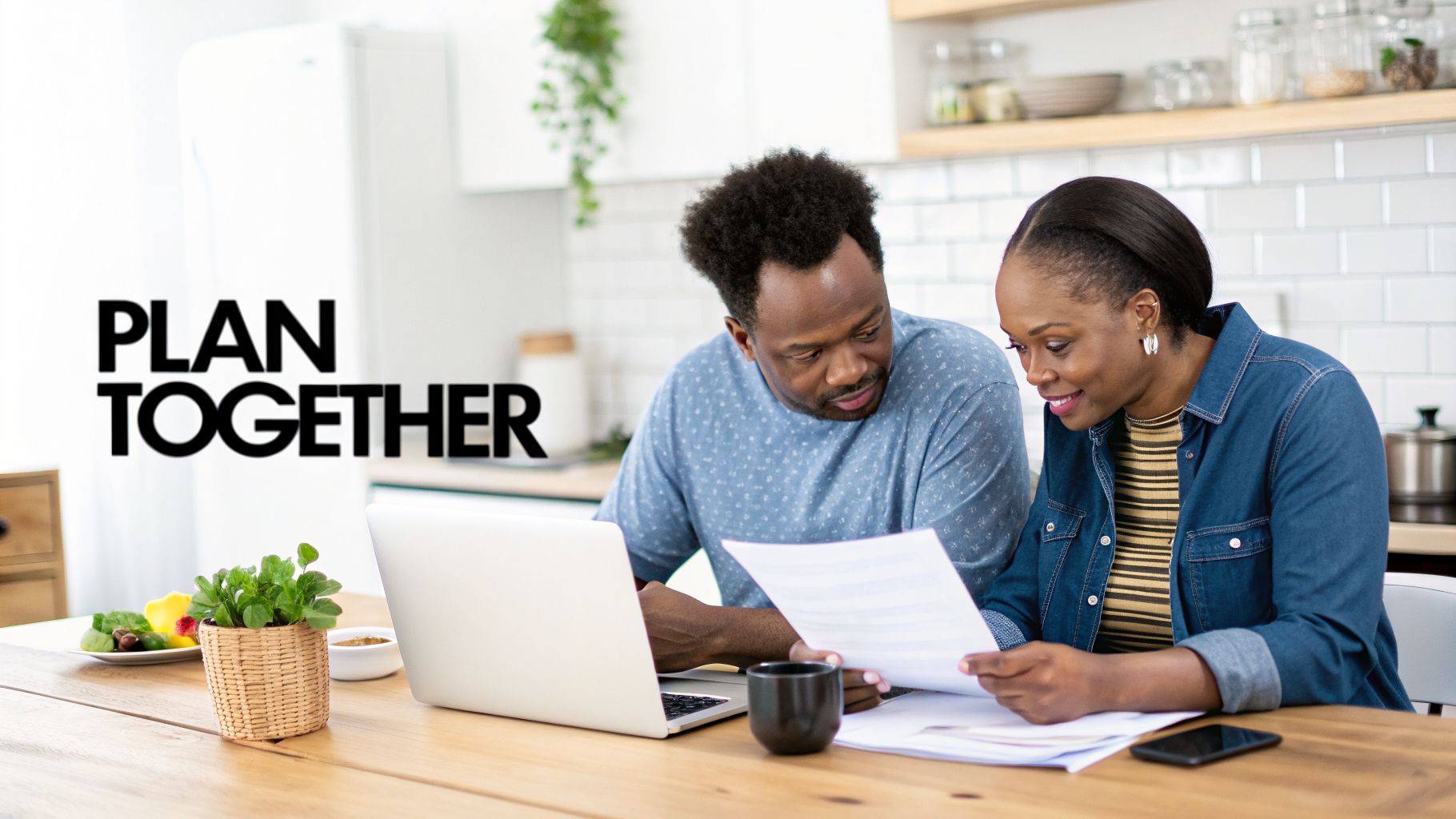 A smiling Black couple at a kitchen table reviews documents and a laptop, planning together.