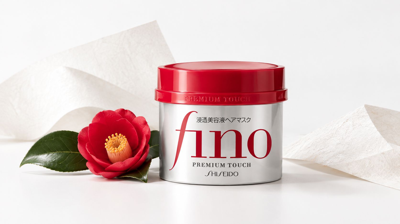 A silver Fino hair mask jar by Shiseido with a red lid beside a vibrant red camellia flower.