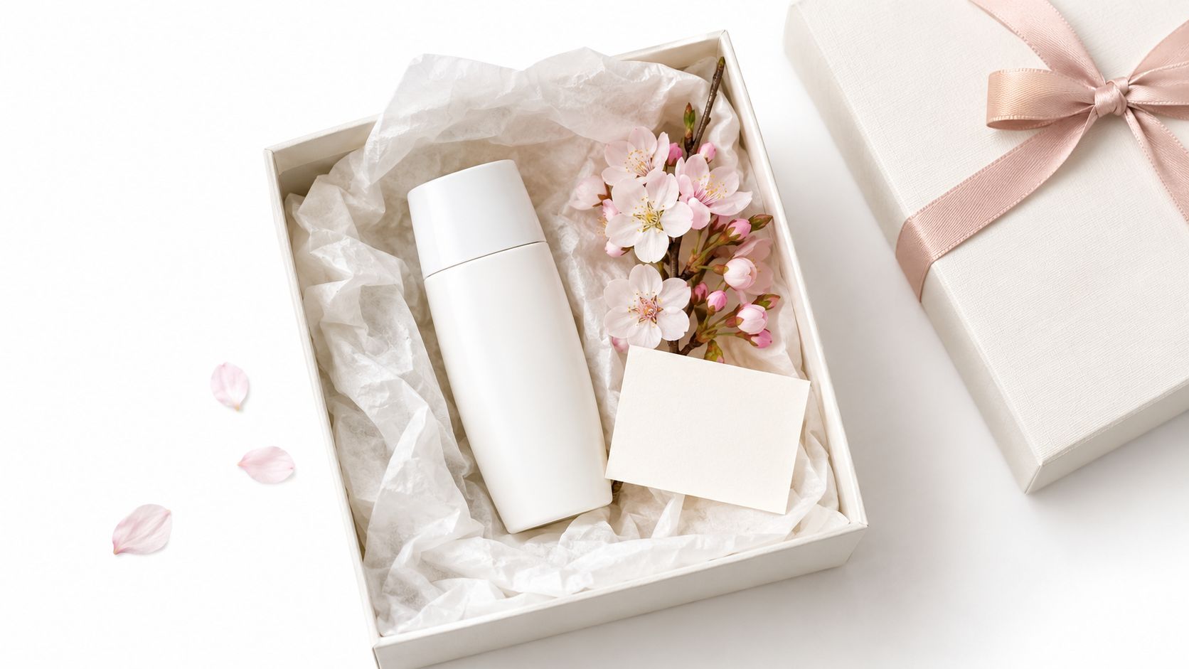 A white sunscreen bottle and cherry blossoms in a gift box with a blank greeting card.