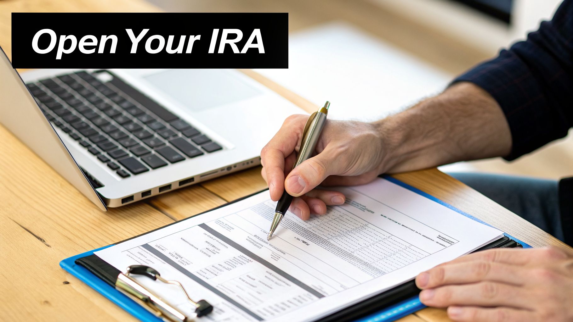 A person is filling out an application form for an IRA account on a wooden desk with a laptop.
