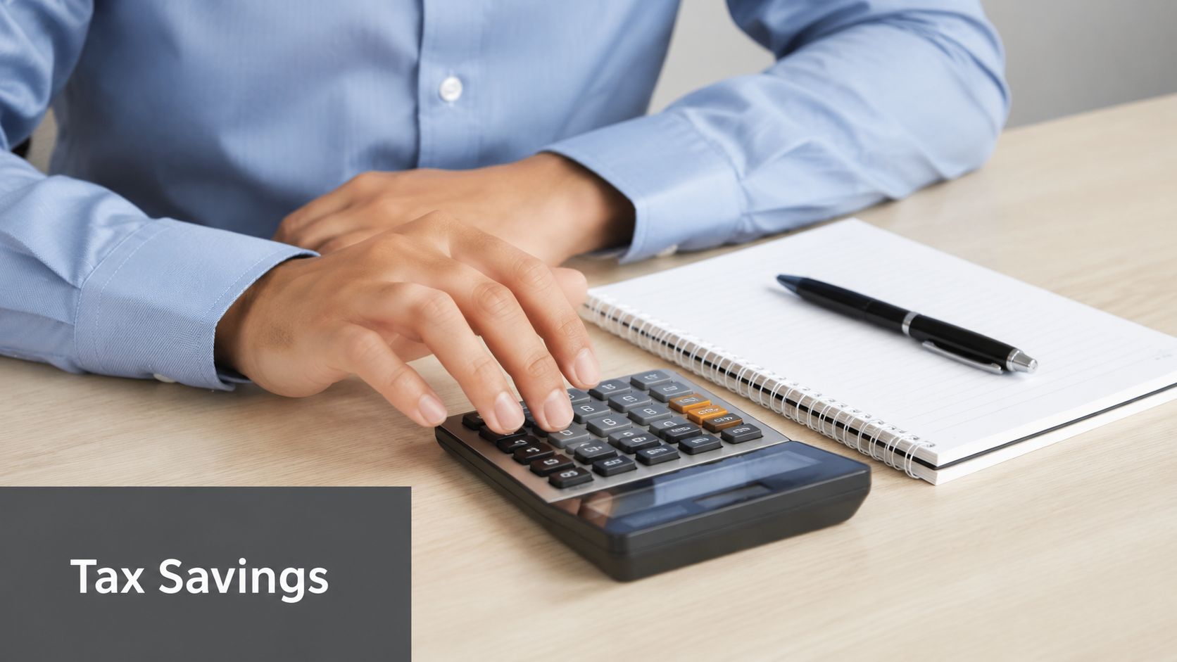 A person in a blue shirt calculating finances with a calculator and notebook on a desk.