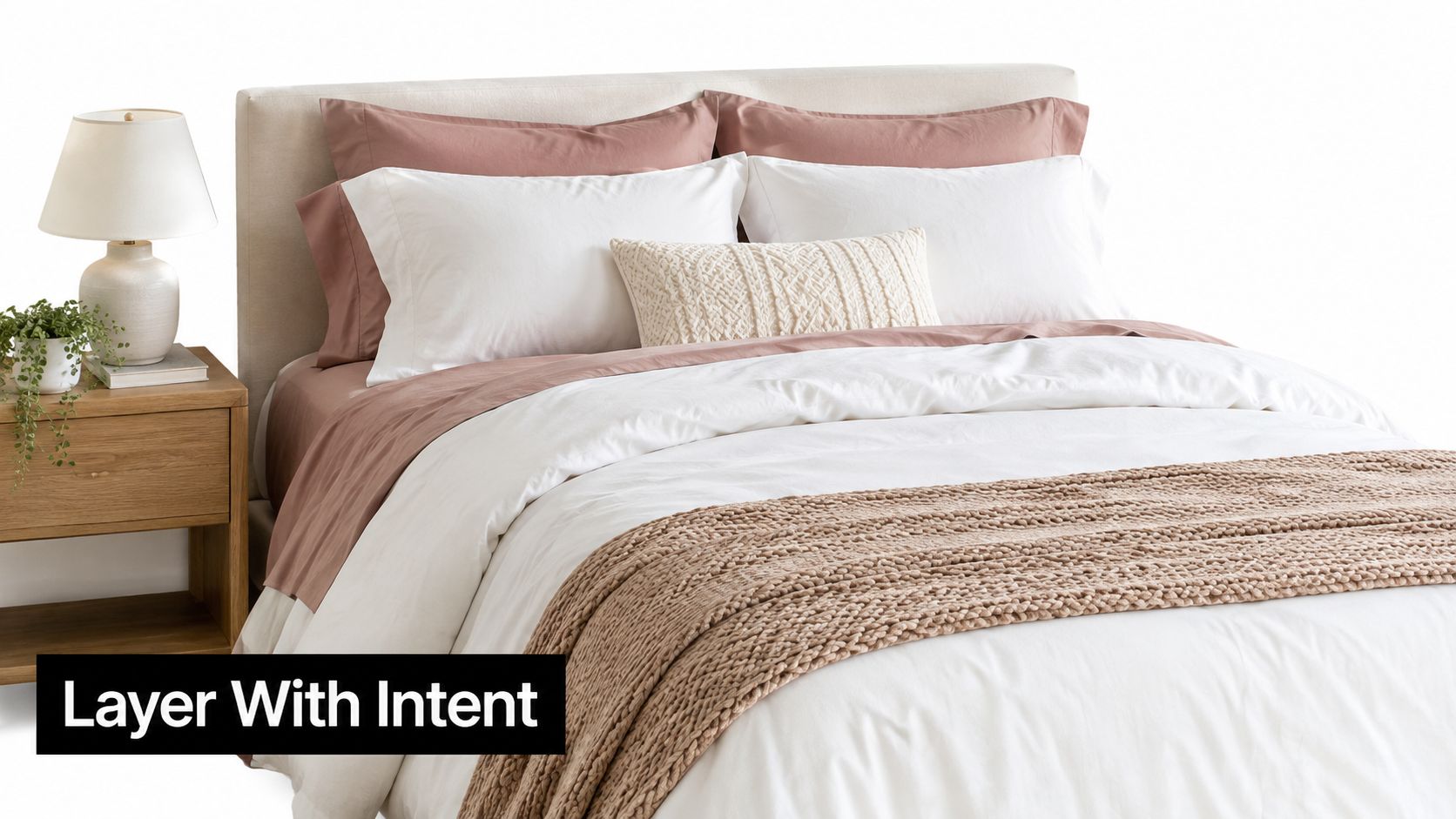 A neatly made bed with dusty rose and white bedding and a chunky knit throw blanket.