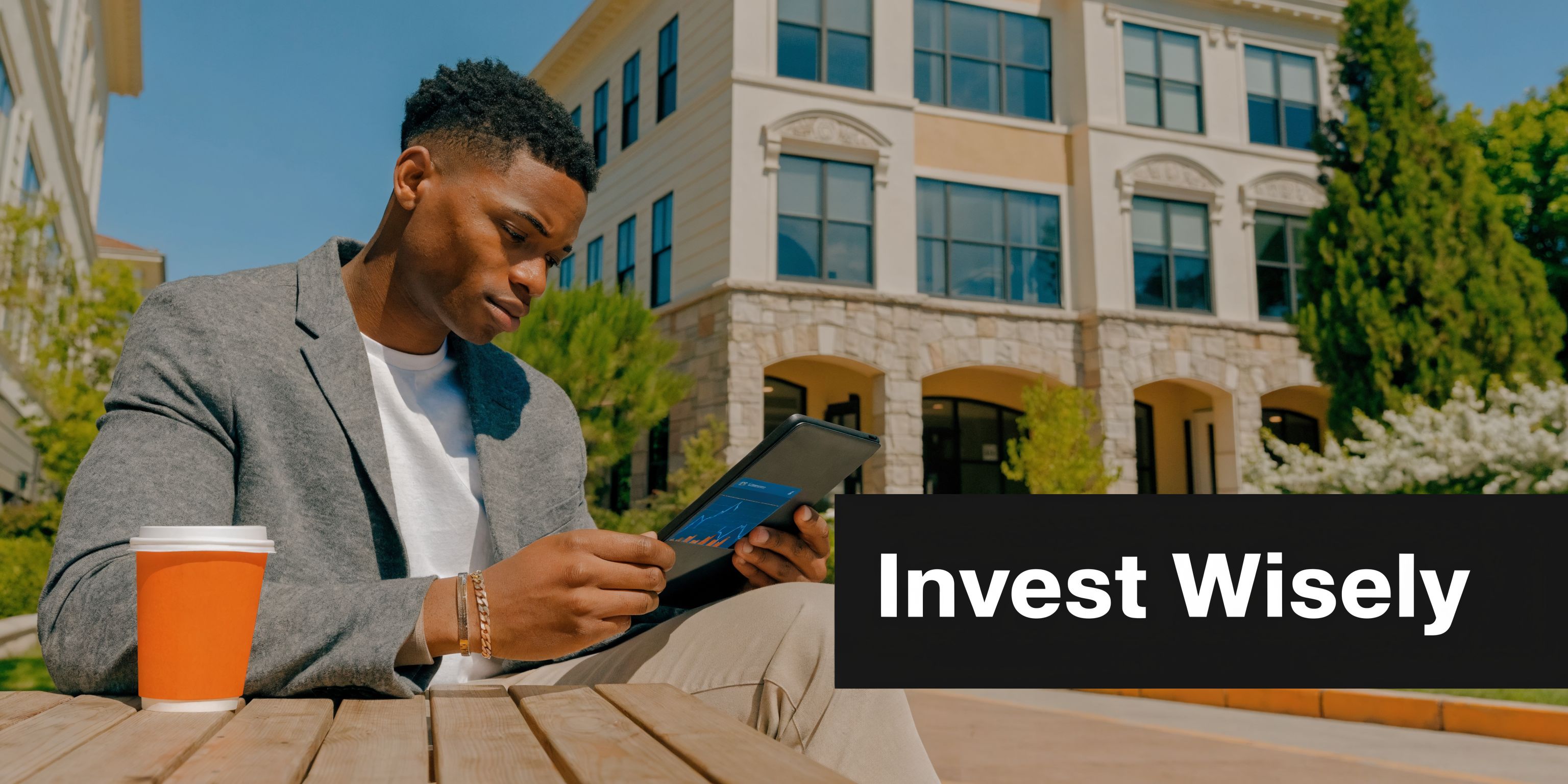 A young professional analyzing financial charts on a tablet while sitting outside near suburban townhouses.
