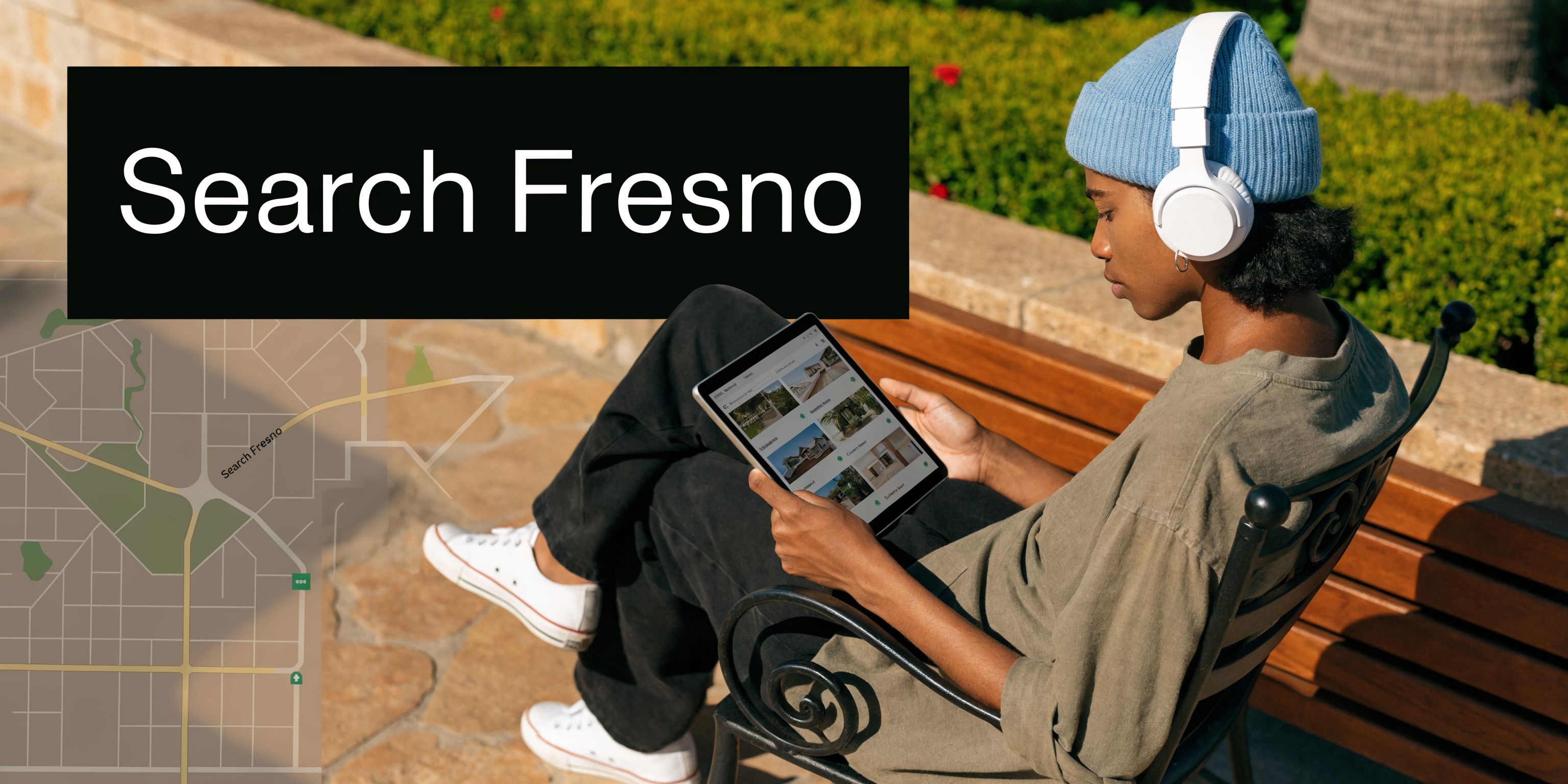 A person wearing a blue beanie and headphones sitting on a bench using a digital tablet outdoors.