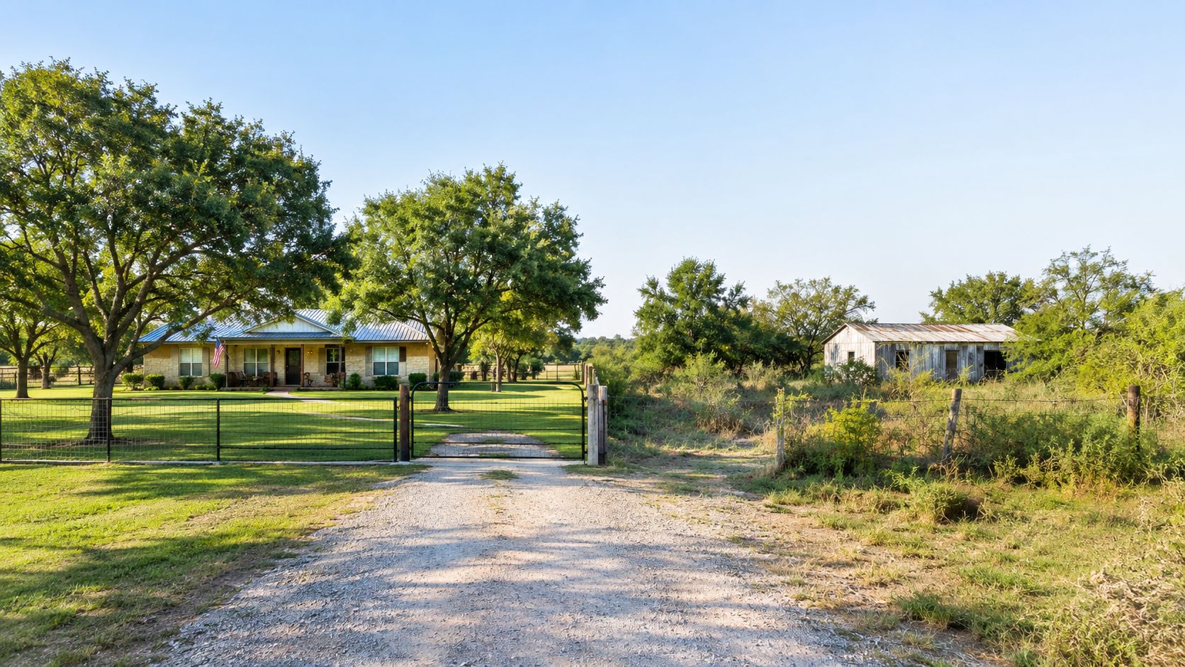 A scenic view of a rural residential property featuring a main house, a barn, and trees.