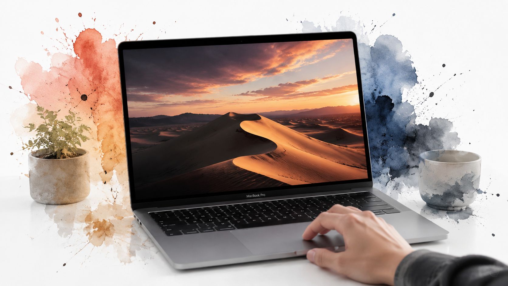 A hand using a silver MacBook Pro with a desert sunset wallpaper on a clean white desk.