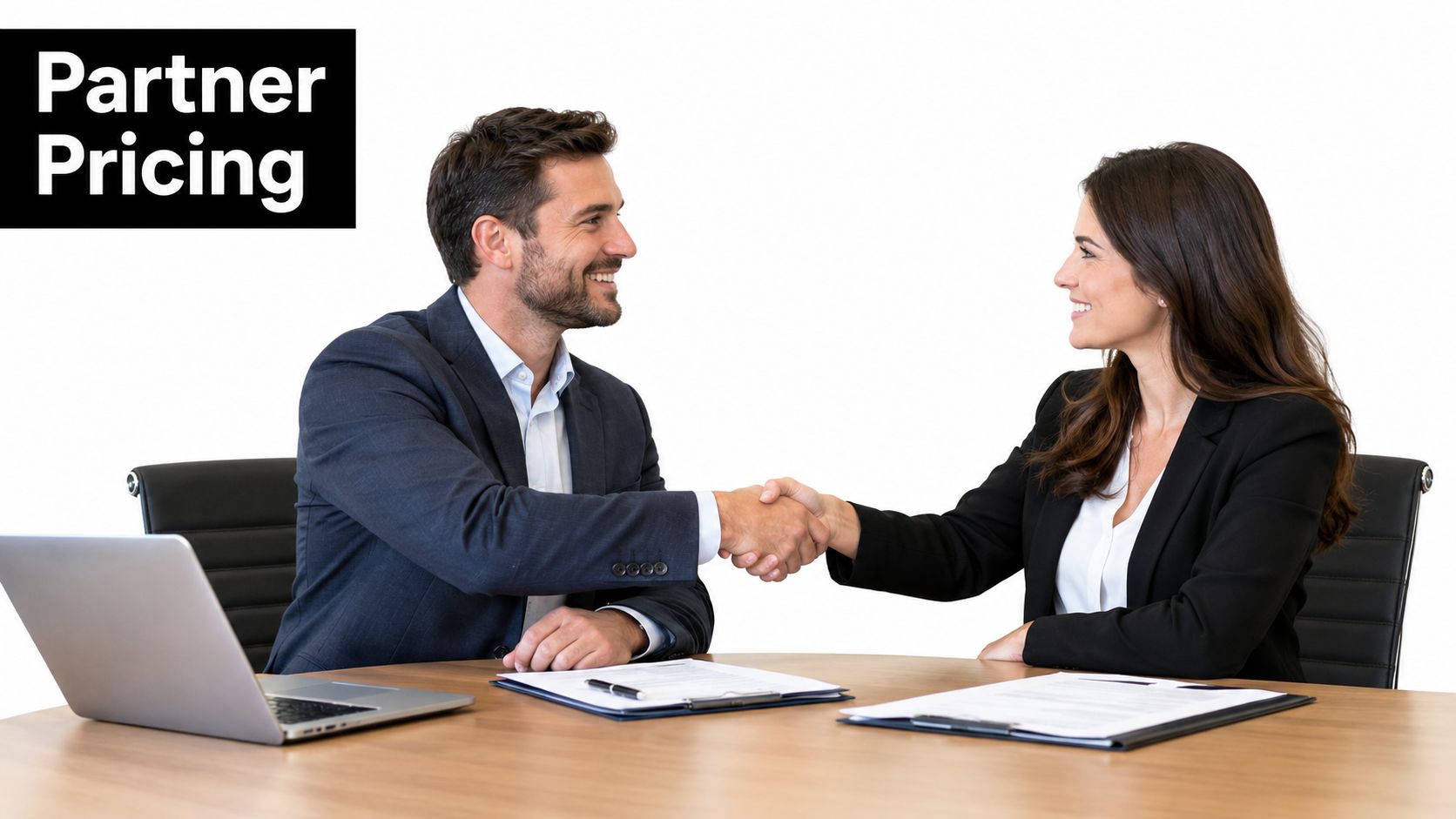A professional man and woman in business attire shaking hands across a desk during a meeting.