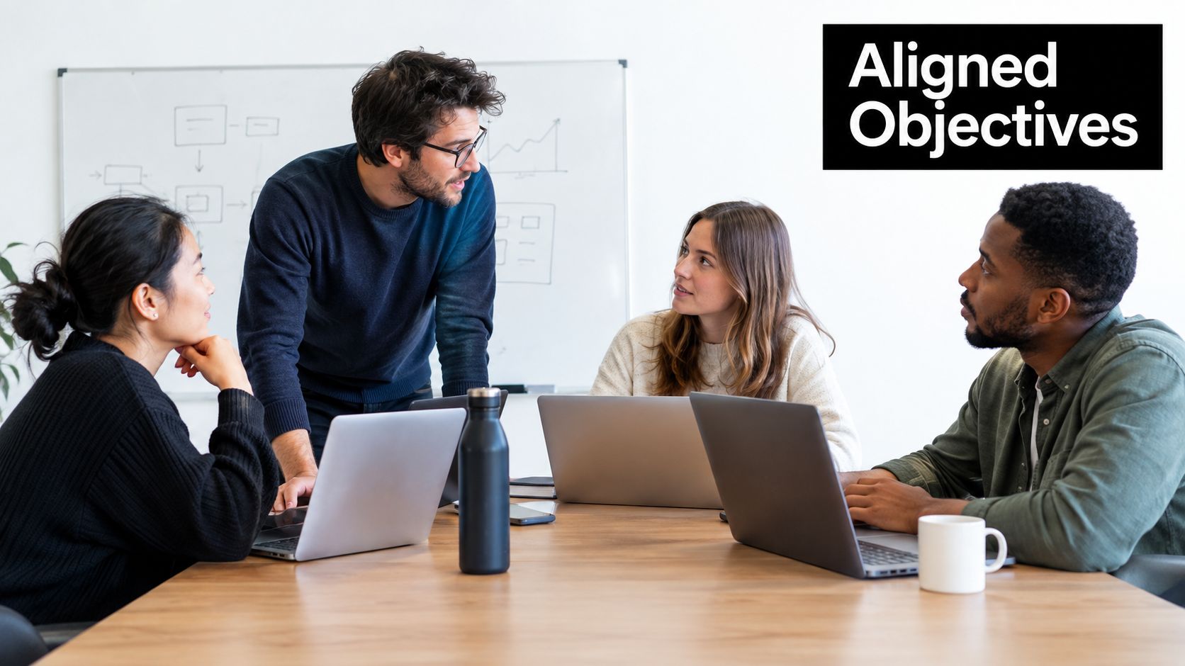 A diverse team of professionals collaborating on business strategy at a table with laptops in an office.
