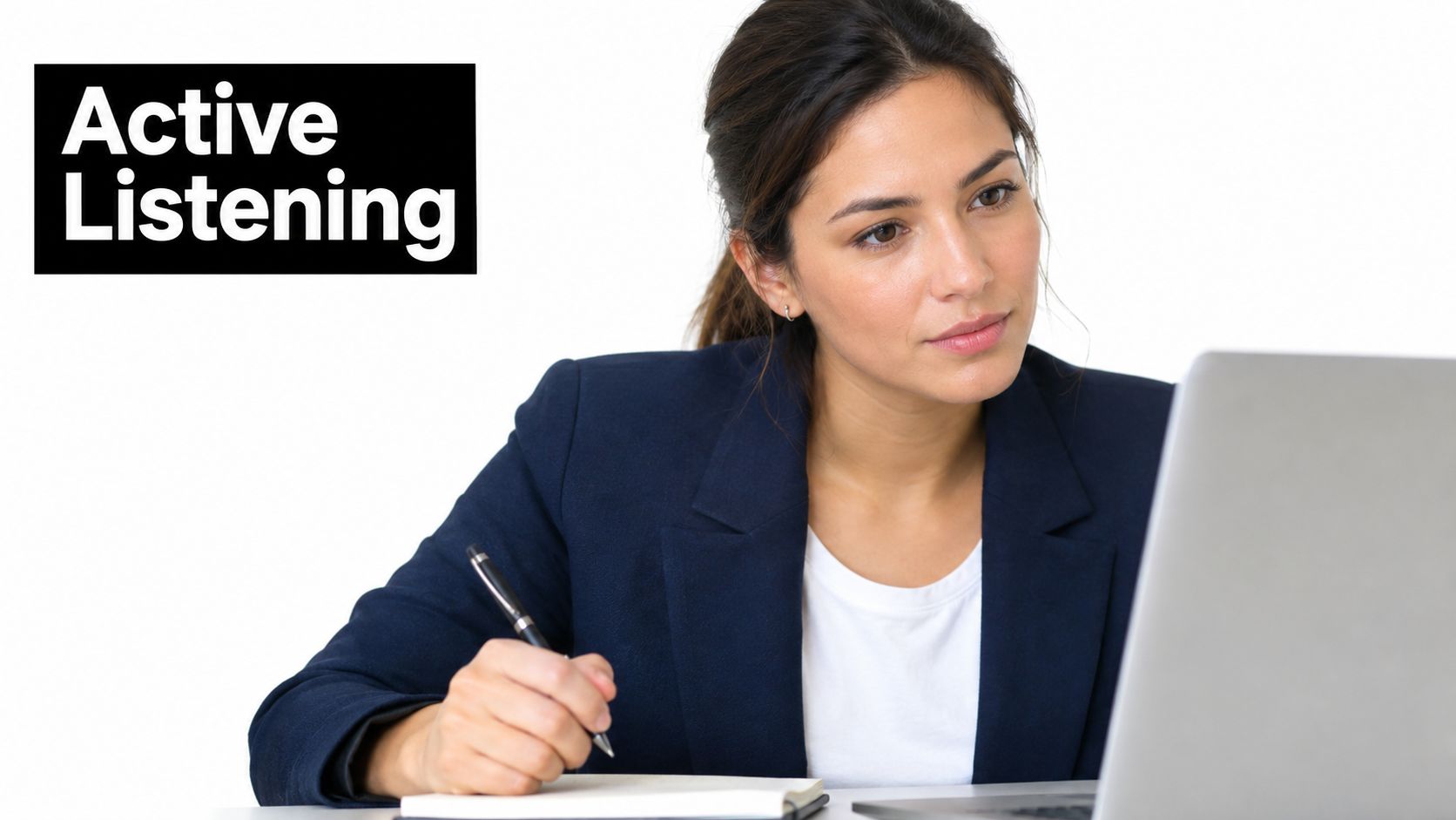 A professional woman in a blazer actively listening and taking notes while looking at her laptop screen.