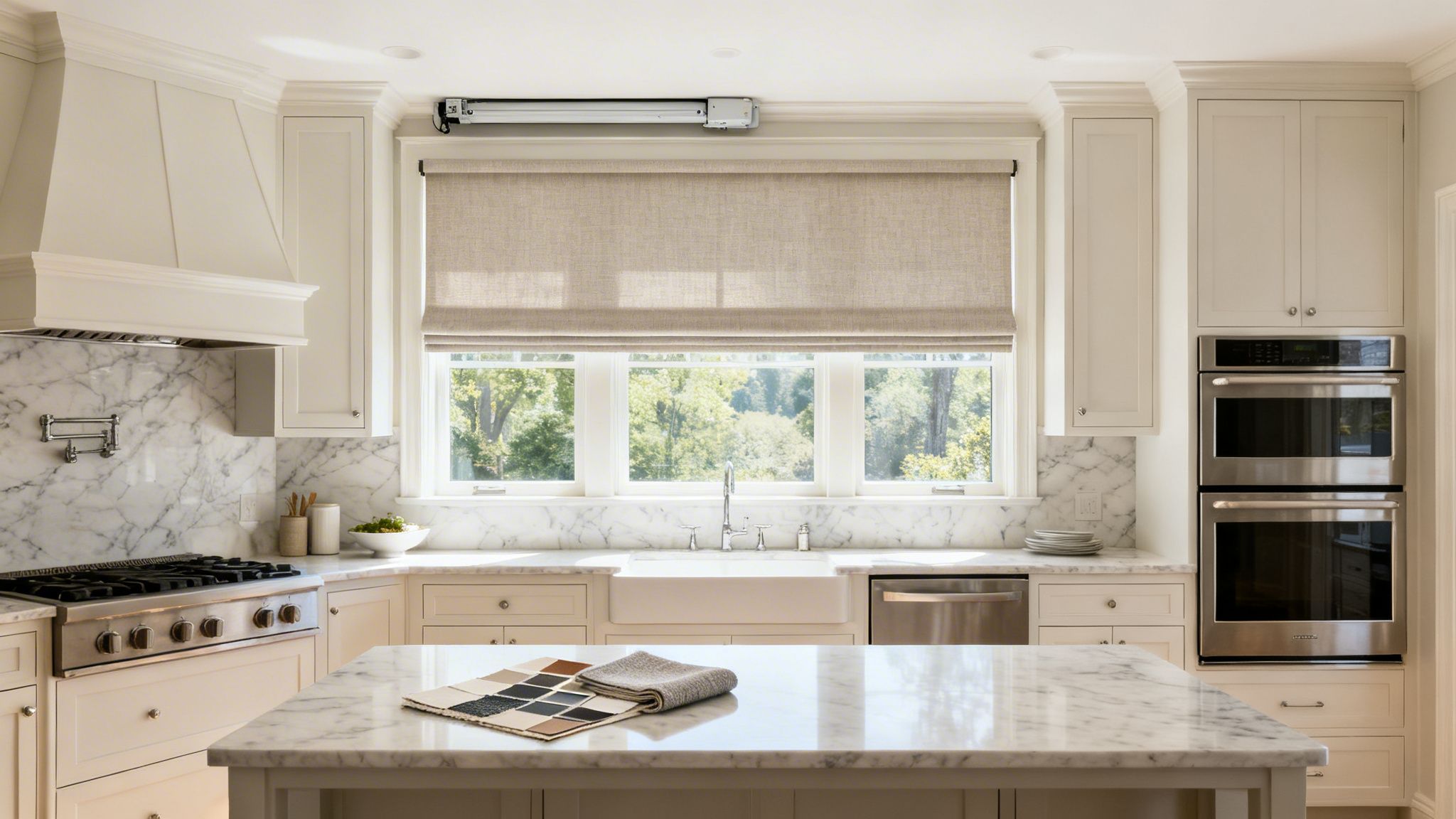 a bright modern kitchen with white cabinets, marble counters, stainless steel appliances, and a roman shade.