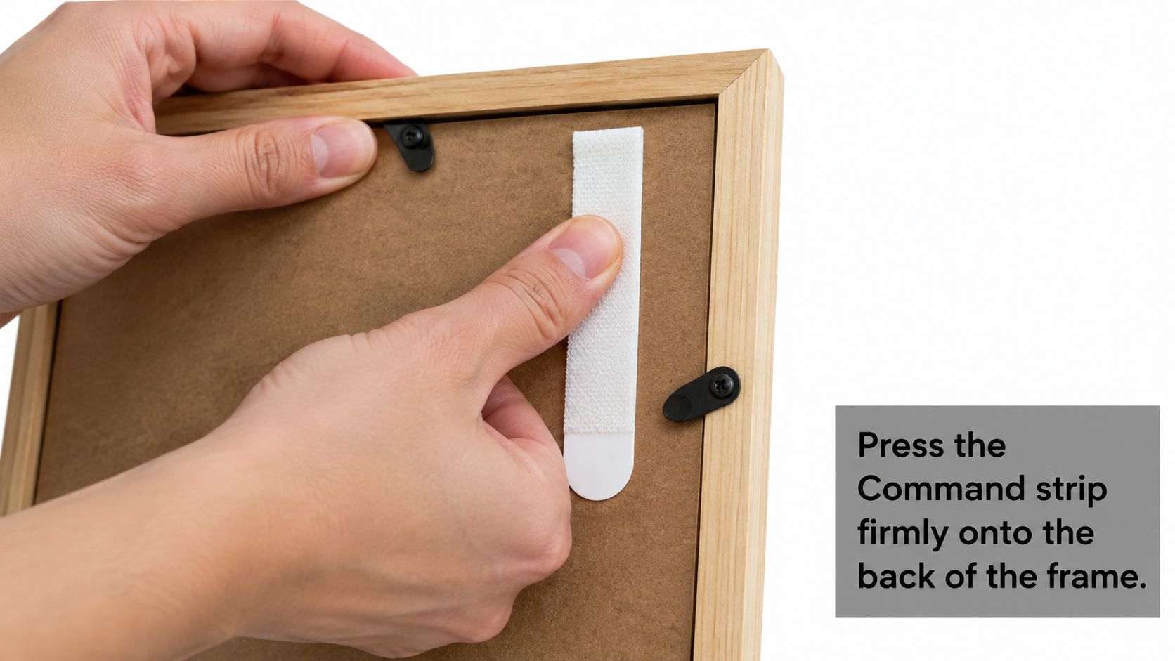A person applying a Command strip adhesive onto the wooden back of a picture frame.