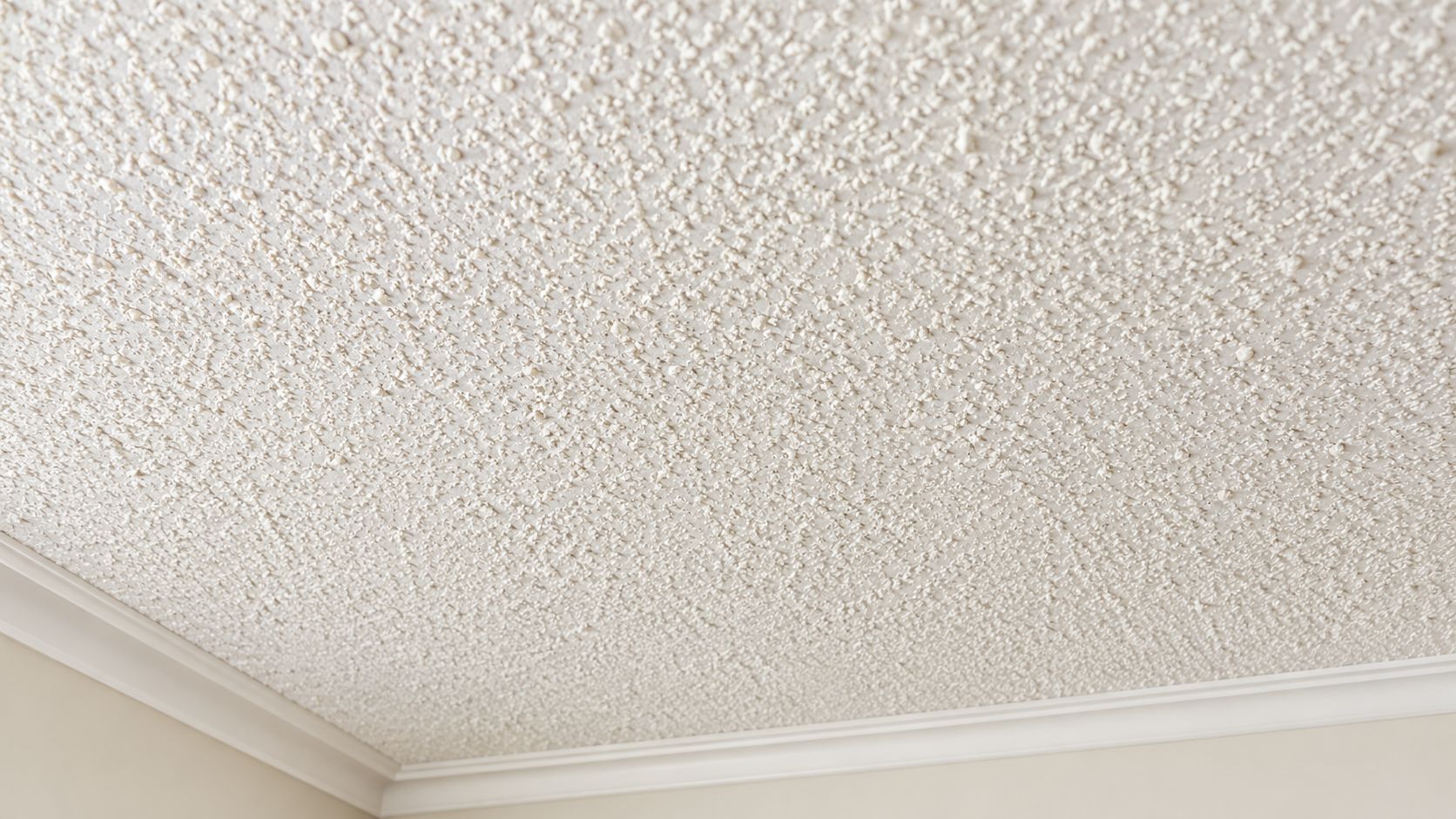 A close-up view of a popcorn textured white ceiling with decorative crown molding in the corner.