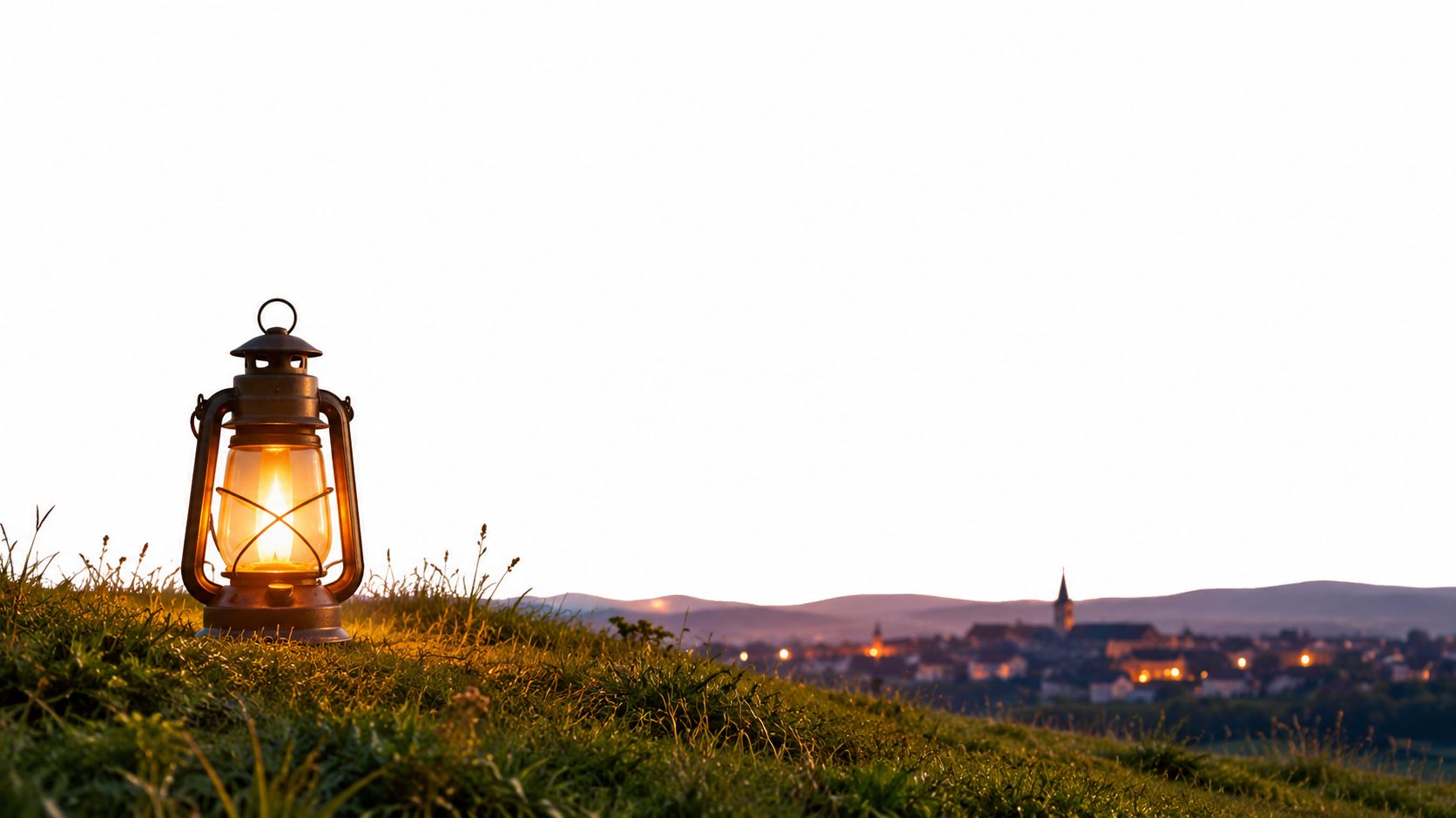 An antique oil lantern glowing on a grassy hill overlooking a small town at sunset.