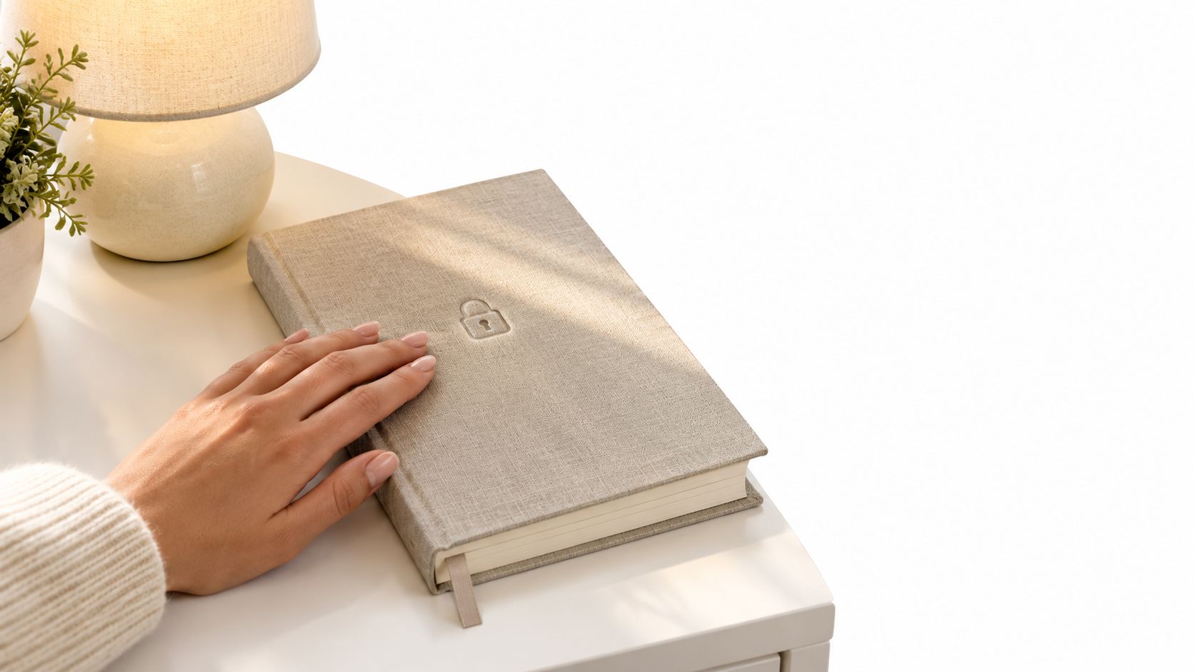 A woman's hand rests gently on a locked beige prayer journal placed on a white bedside table.