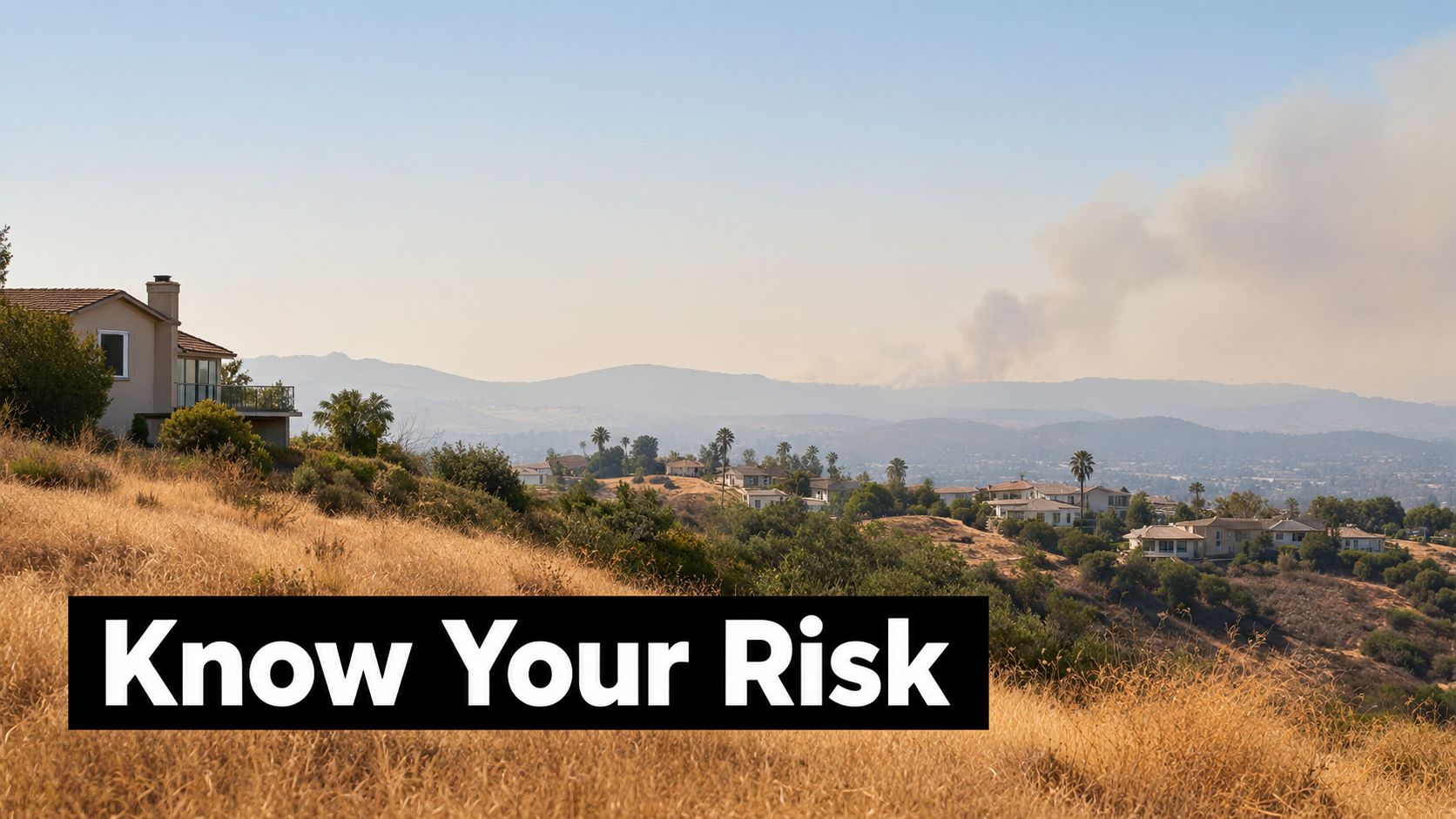 A scenic view of homes on a dry, grassy hill with wildfire smoke rising in the distance.
