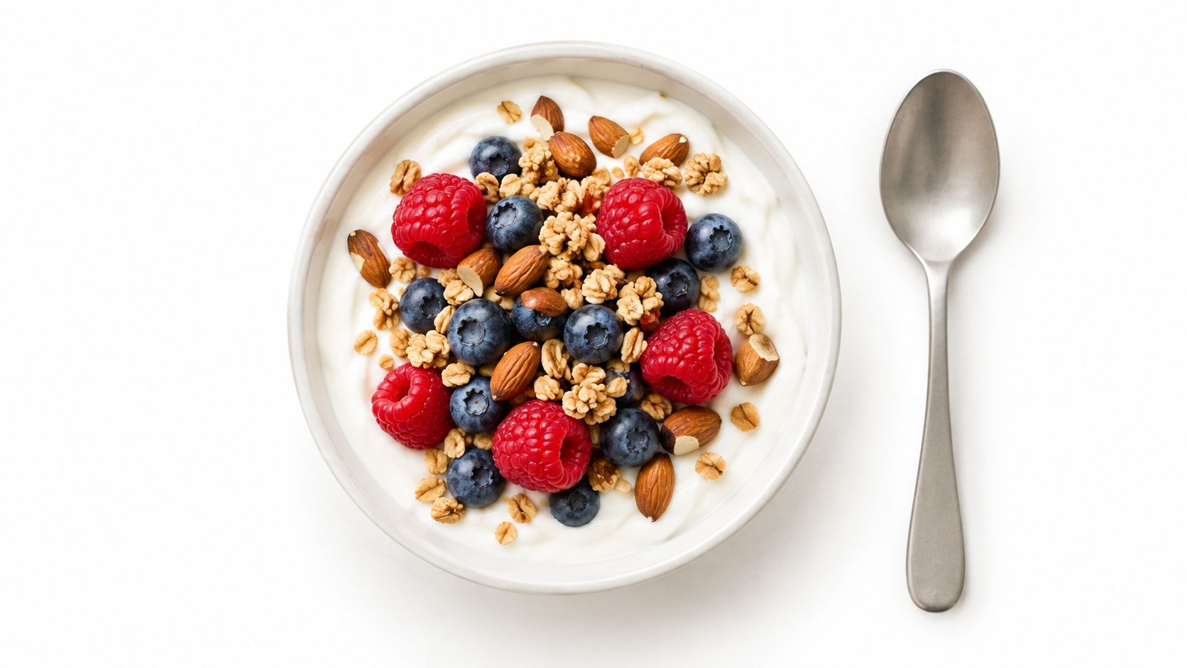 A top-down view of a bowl of yogurt topped with fresh berries, crunchy granola, and almonds.