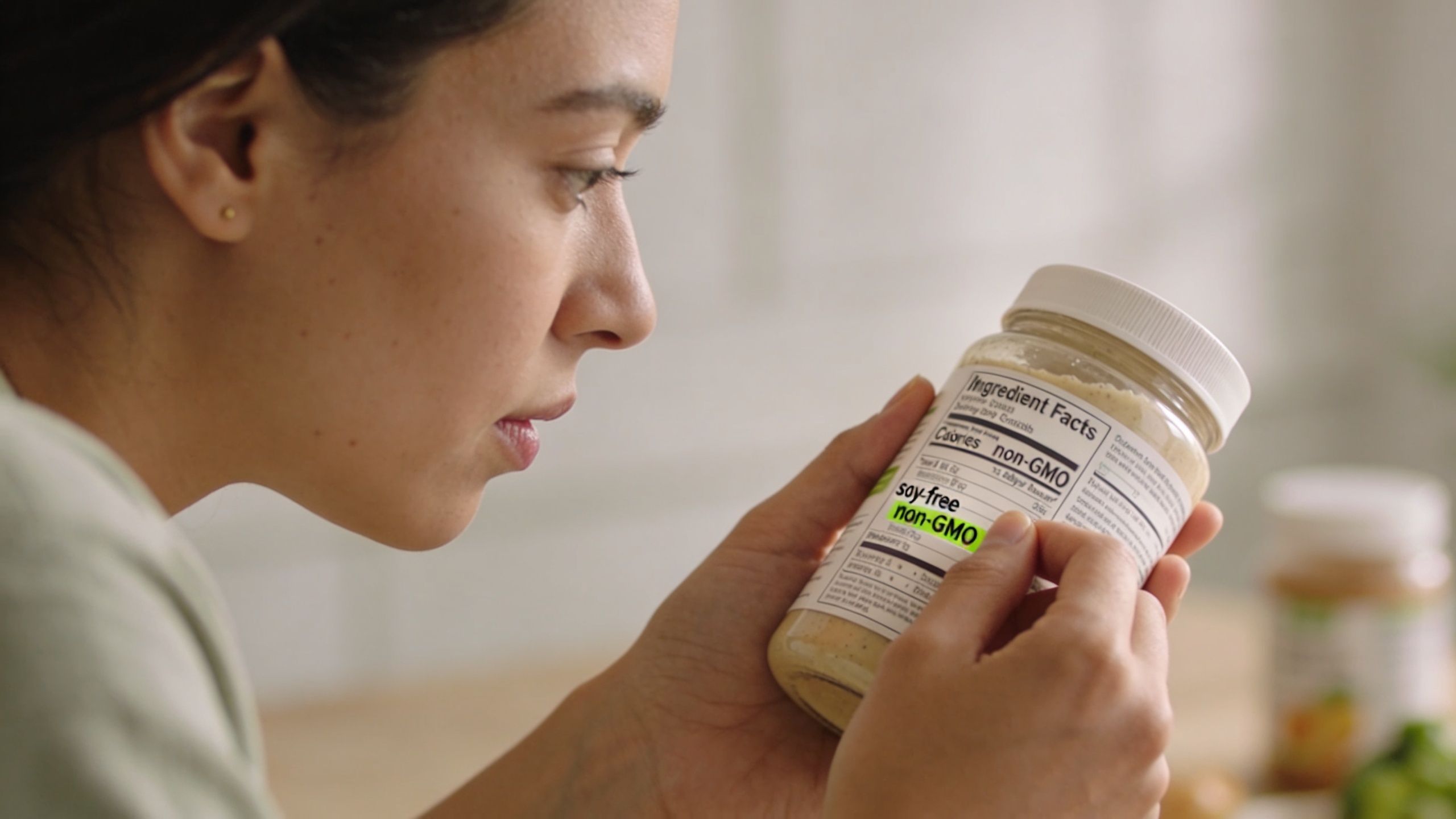 A woman inspecting the ingredients label on a jar to ensure it is soy-free and non-GMO.