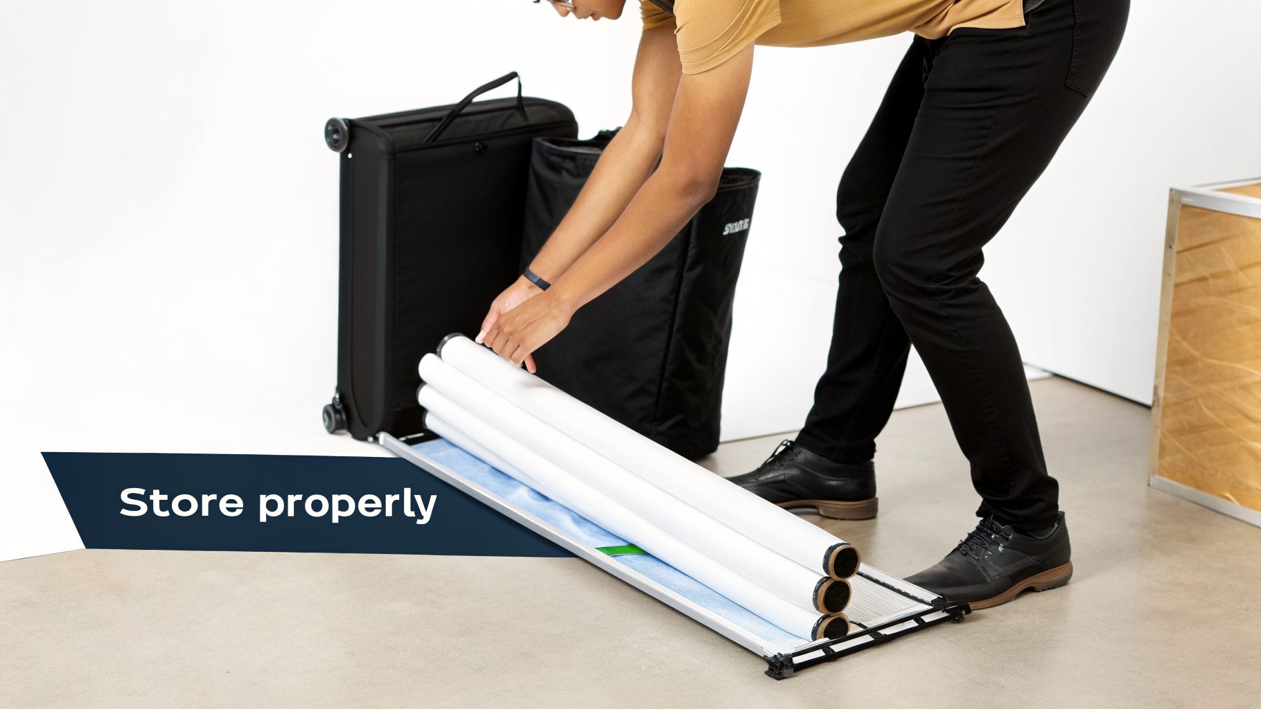 A person carefully places rolled-up white banner graphics onto a display stand for proper storage.