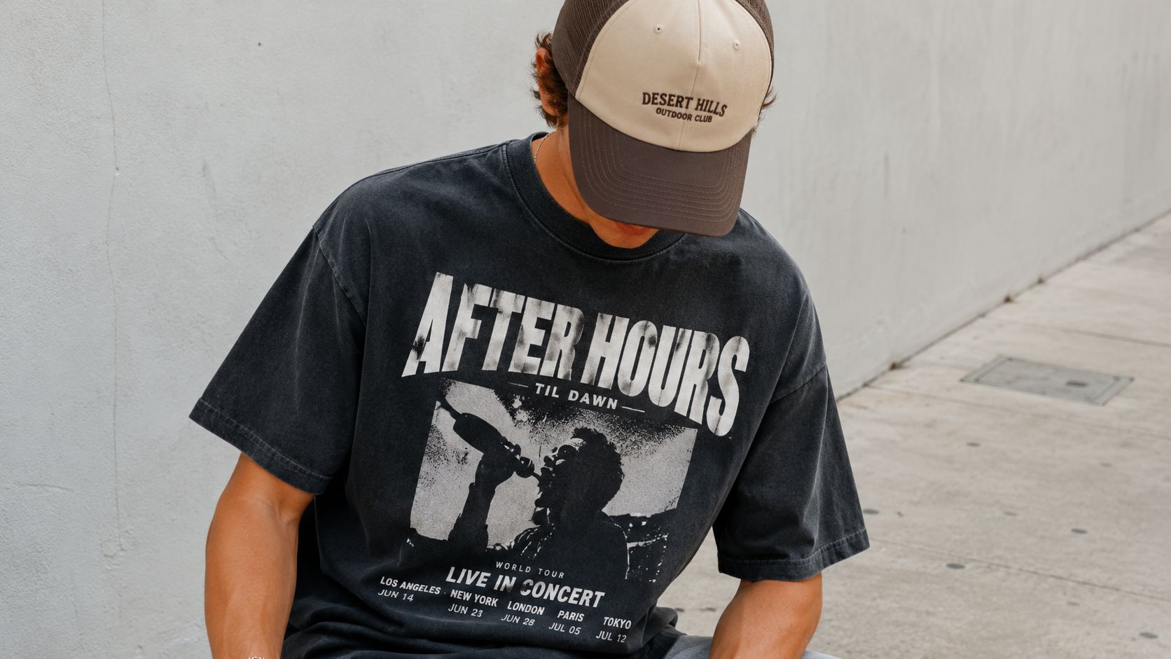 A person wearing a vintage-style graphic After Hours tour t-shirt and a Desert Hills baseball cap.
