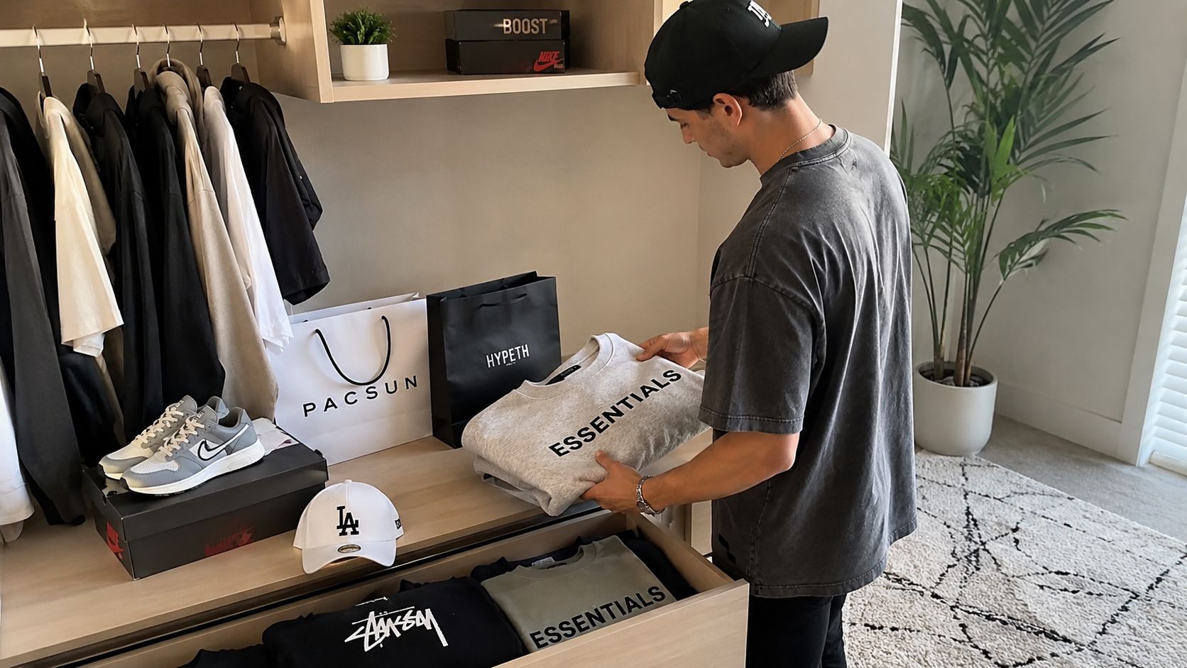 A young man organizing his closet filled with trendy online streetwear brands and clothing items.