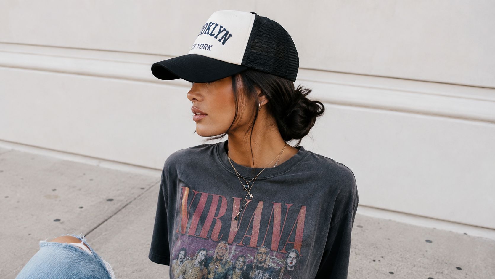 A woman wearing a black and white Brooklyn trucker hat and a vintage Nirvana band t-shirt.
