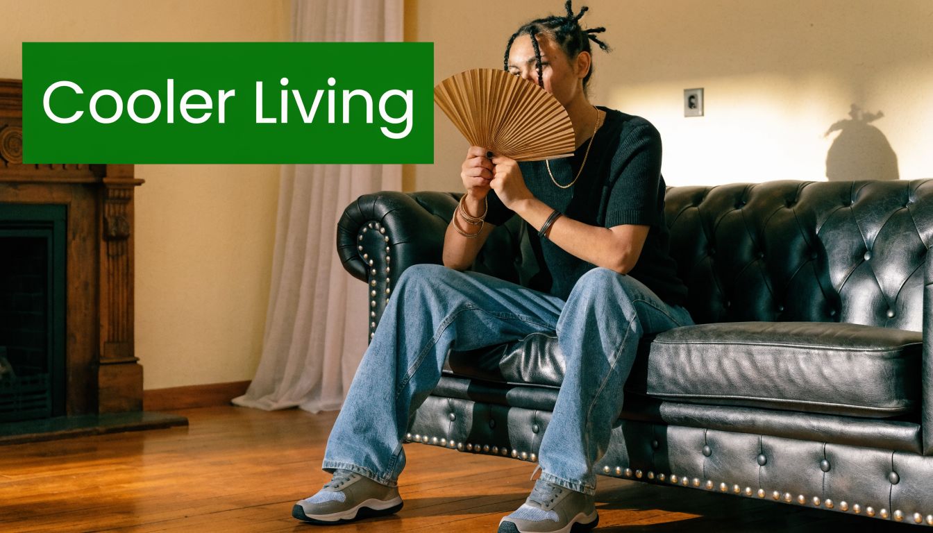 A person sitting on a dark leather couch holding a paper hand fan to stay cool indoors.
