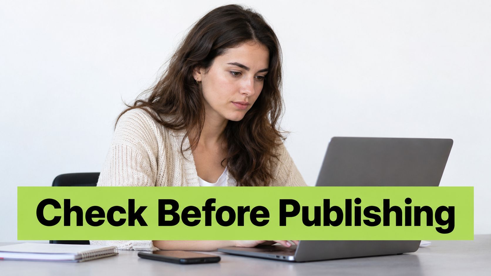 A focused woman sitting at a desk and working on her laptop while reviewing digital content.