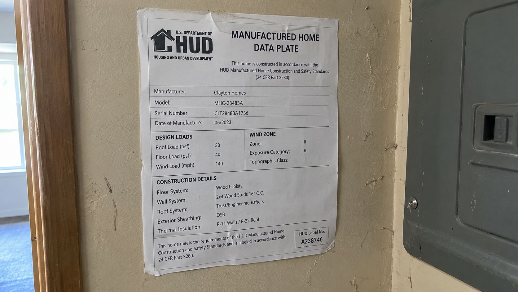 A HUD manufactured home data plate sticker posted on a wall listing home construction and safety standards.