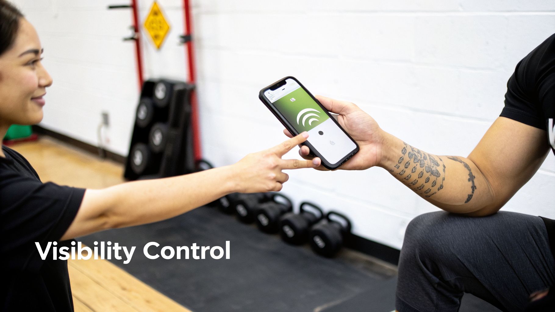 Two individuals interact with a smartphone showing a green app, likely controlling discoverable mode in a gym.
