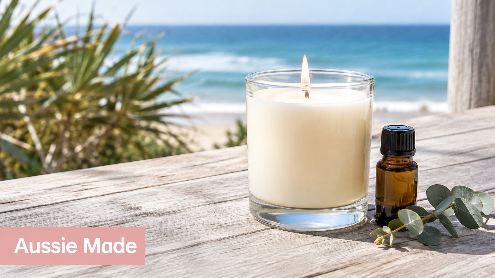 A lit glass candle and essential oil bottle on a wooden deck by the Australian beach.