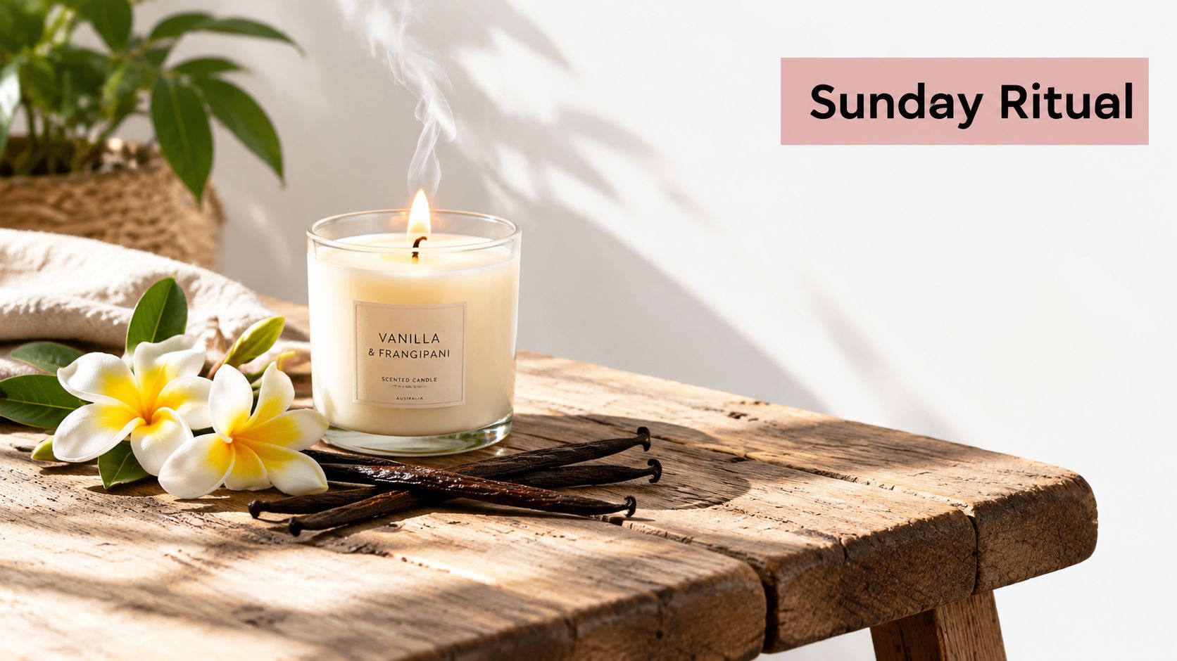 A burning vanilla and frangipani scented candle placed on a rustic wooden table with frangipani flowers and vanilla beans.