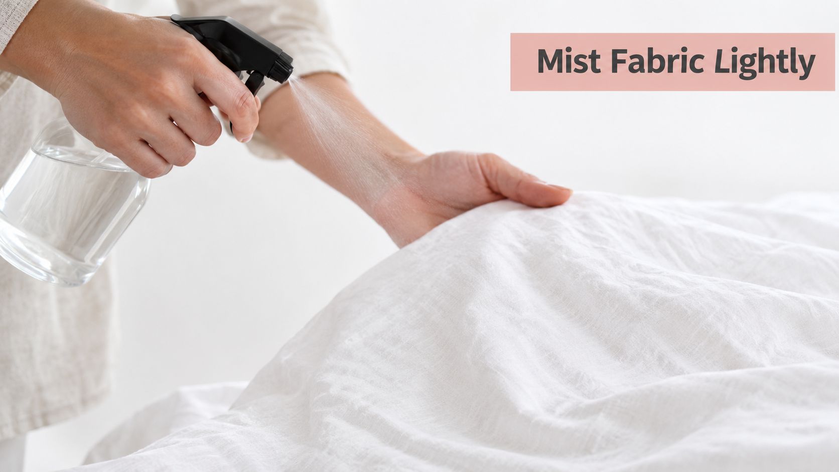A person lightly misting a white linen fabric with a clear spray bottle to refresh it.