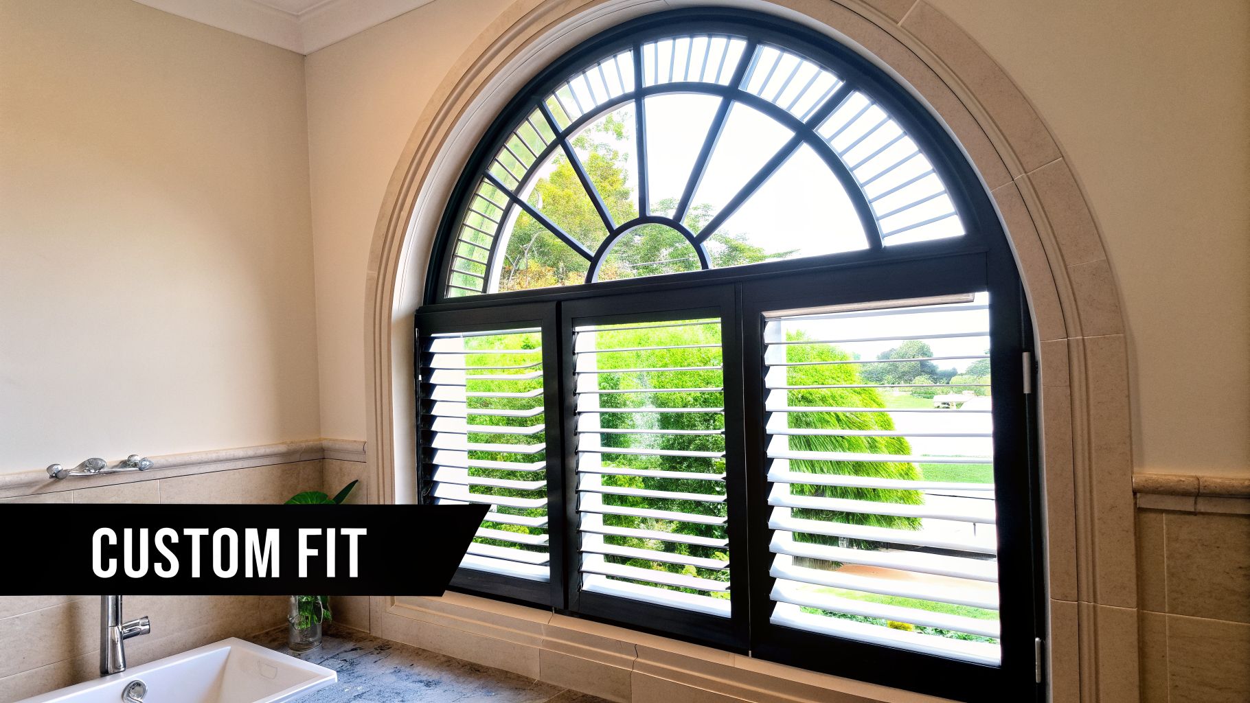 Elegant arched window with custom-fit black plantation shutters, offering a view of lush green trees.